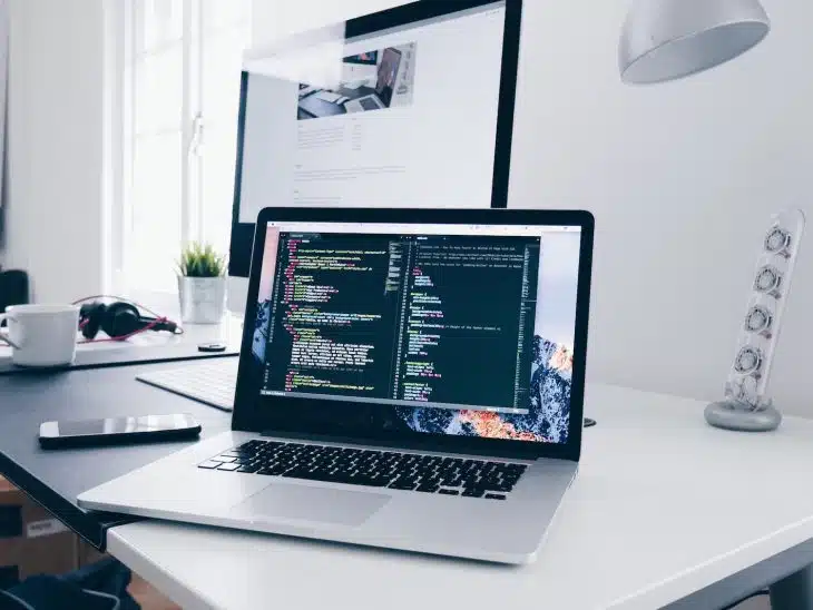 A MacBook with lines of code on its screen on a busy desk